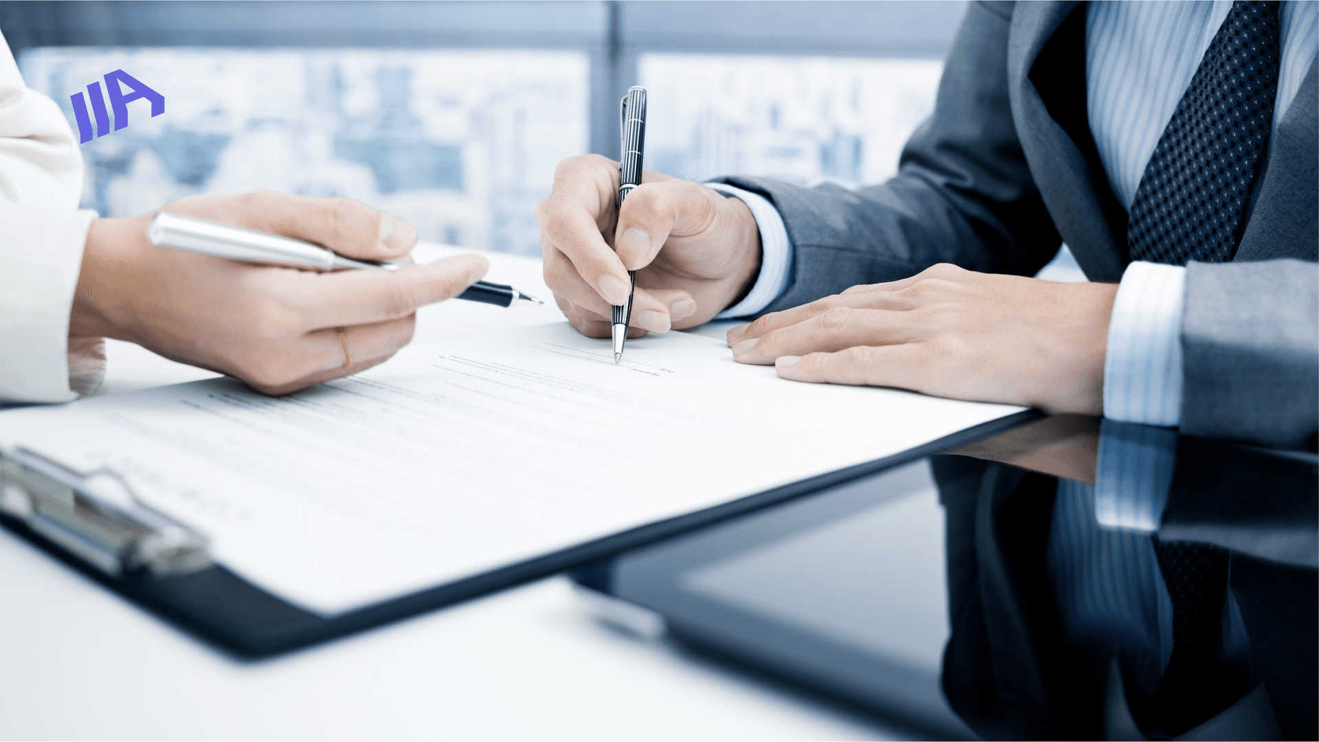 Two individuals signing a document at a desk, with professional attire and pens in hand.